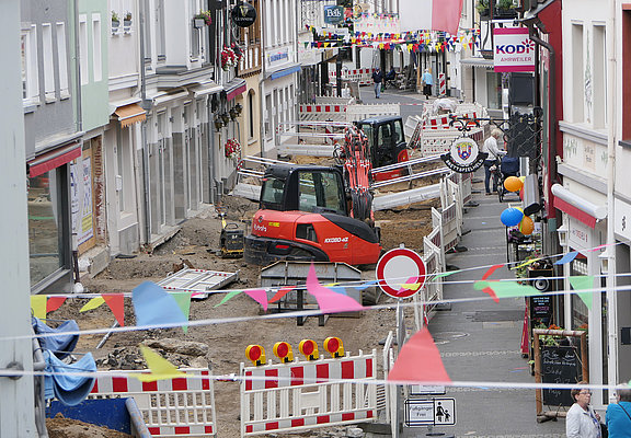 Baustelle in der Innenstadt von Ahrweiler im Stadtteil Ahrweiler mit Baufahrzeugen, Straßensperrungen und bunten Fahnen im Vordergrund.