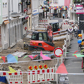 Baustelle in der Innenstadt von Ahrweiler im Stadtteil Ahrweiler mit Baufahrzeugen, Straßensperrungen und bunten Fahnen im Vordergrund.