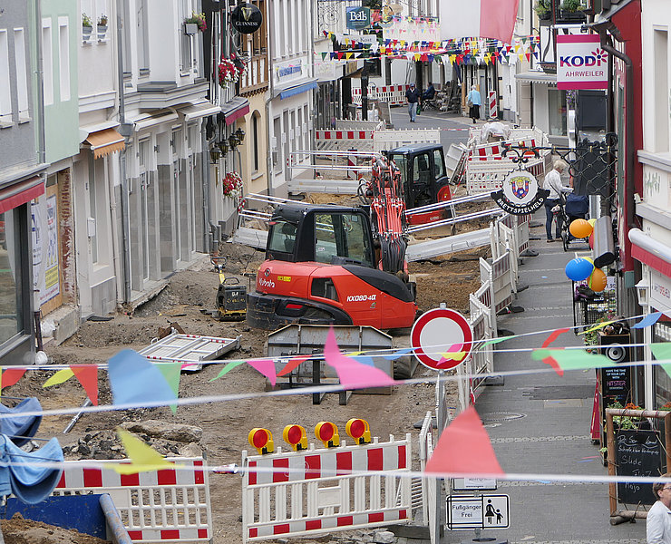 Baustelle in der Innenstadt von Ahrweiler im Stadtteil Ahrweiler mit Baufahrzeugen, Straßensperrungen und bunten Fahnen im Vordergrund.