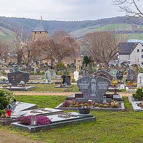 Blick über den Ahrtor-Friedhof im Stadtteil Ahrweiler mit historischen Gebäuden und Weinbergen im Hintergrund.