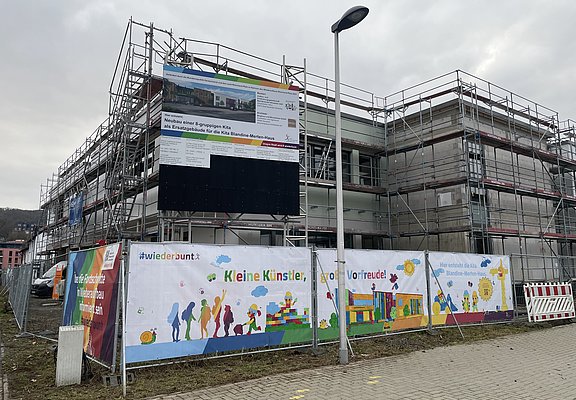 Bunte Farben auf einem Banner hängen vor dem Gerüst des Kita-Neubaus