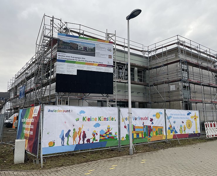 Bunte Farben auf einem Banner hängen vor dem Gerüst des Kita-Neubaus