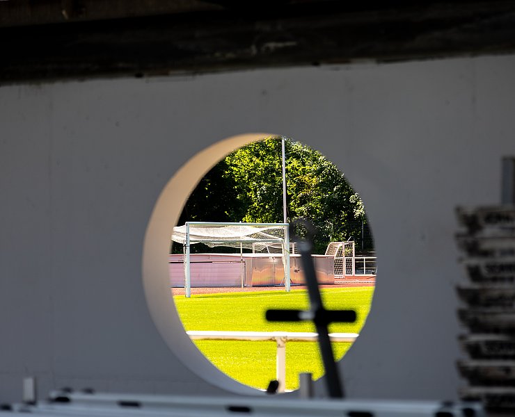 Blick durch eine runde Öffnung auf das noch im Bau befindliche Apollinarisstadion im Stadtteil Bad Neuenahr.