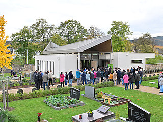 Besucher vor der modernen Aussegnungshalle auf dem Friedhof im Stadtteil Ahrweiler, umgeben von Gräbern und grüner Anlage.