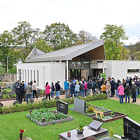 Besucher vor der modernen Aussegnungshalle auf dem Friedhof im Stadtteil Ahrweiler, umgeben von Gräbern und grüner Anlage.