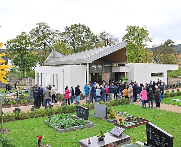Besucher vor der modernen Aussegnungshalle auf dem Friedhof im Stadtteil Ahrweiler, umgeben von Gräbern und grüner Anlage.