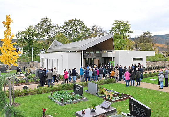 Besucher vor der modernen Aussegnungshalle auf dem Friedhof im Stadtteil Ahrweiler, umgeben von Gräbern und grüner Anlage.
