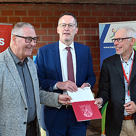 Drei Männer übergeben Unterlagen zum Neubau der Kita St. Hildegard im Stadtteil Bad Neuenahr, Ahrtal.