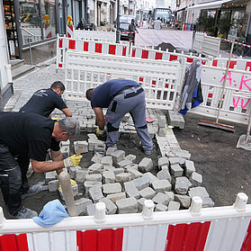 Mehrere Arbeiter auf der Baustelle bei Pflasterabeiten.