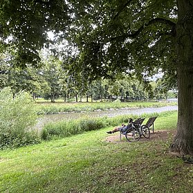 Ein Mann sitzt auf einer ergonomischen Holzbank und blickt auf die Ahr. Sein Fahrrad ist an die Bank angelehnt.