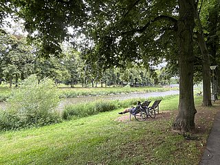 Ein Mann sitzt auf einer ergonomischen Holzbank und blickt auf die Ahr. Sein Fahrrad ist an die Bank angelehnt.