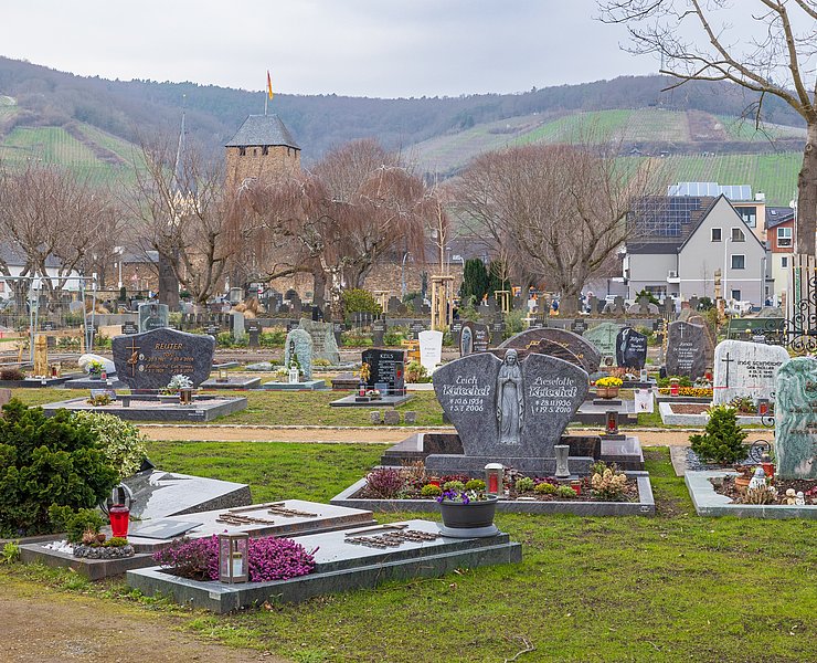 Blick über den Ahrtor-Friedhof im Stadtteil Ahrweiler mit historischen Gebäuden und Weinbergen im Hintergrund.