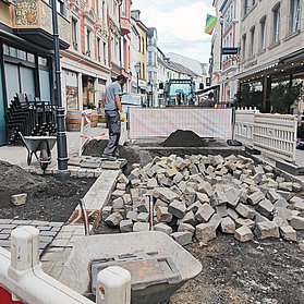 Lose Pflastersteine auf der Baustelle in der Niederhut, mit rot-weißer Bausperrung im Vordergrund.