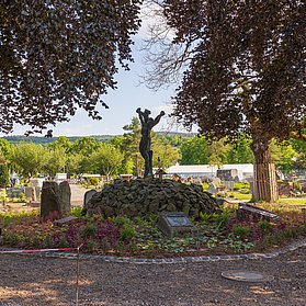 Ahrtor-Friedhof in Ahrweiler mit zentralem Denkmal, umgeben von Bäumen und Gräbern im Stadtteil Ahrweiler.