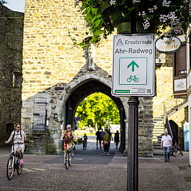 Ersatzroute des Ahr-Radwegs am historischen Stadttor in Bad Neuenahr-Ahrweiler mit Radfahrern und Fußgängern.