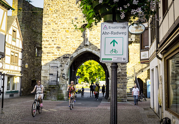 Ersatzroute des Ahr-Radwegs am historischen Stadttor in Bad Neuenahr-Ahrweiler mit Radfahrern und Fußgängern.