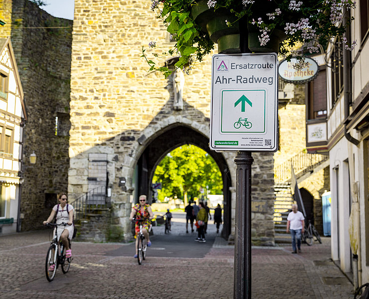 Ersatzroute des Ahr-Radwegs am historischen Stadttor in Bad Neuenahr-Ahrweiler mit Radfahrern und Fußgängern.