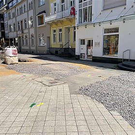 Asphalt und lockerer Boden mit bunten Fußabdrücken, die Richtung Einzelhandel führen.