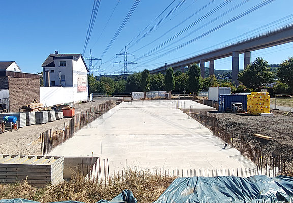Fundament des Neubaus neben Wohnhäusern und Brücke.
