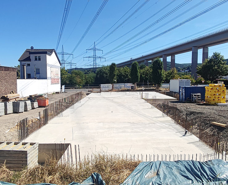 Fundament des Neubaus neben Wohnhäusern und Brücke.