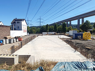 Fundament des Neubaus neben Wohnhäusern und Brücke.