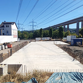 Fundament des Neubaus neben Wohnhäusern und Brücke.