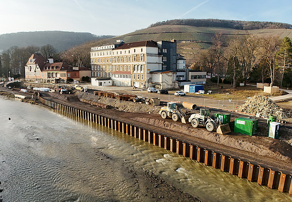 Bauarbeiten an der Carl-von-Ehrenwall-Allee in Ahrweiler mit Baumaschinen und Uferbefestigung am Fluss.