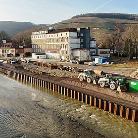 Bauarbeiten an der Carl-von-Ehrenwall-Allee in Ahrweiler mit Baumaschinen und Uferbefestigung am Fluss.