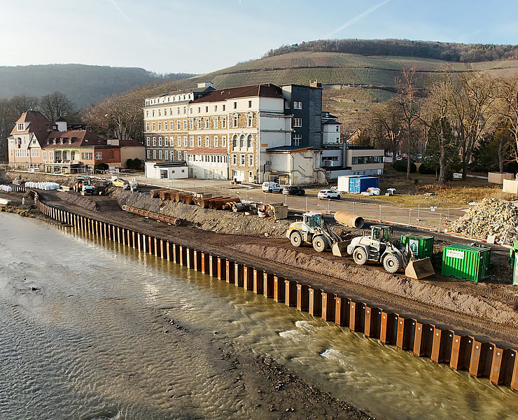 Bauarbeiten an der Carl-von-Ehrenwall-Allee in Ahrweiler mit Baumaschinen und Uferbefestigung am Fluss.
