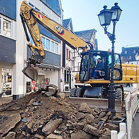 Offene Baustelle mit Bagger und begehbarem Streifen an der Seite.