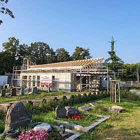 Aussegnungshalle im Bau auf dem Friedhof Ahrweiler, umgeben von bunten Gräbern und Grünflächen.