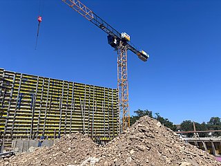 Eine erste Trennwand vor einem Kran sichtbar. Im Vordergrund ist ein Erdhaufen.