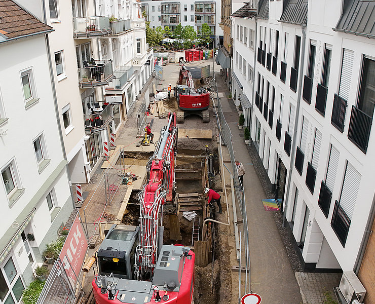 Bagger arbeiten an offener Straße zwischen Wohnhäusern