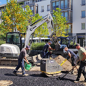Arbeiter bereiten den Asphalt vor, begleitet von einem Bagger.