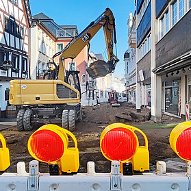 Bagger schaufelt Erde in der Niederhut mit Sicherheitsabsperrungen im Vordergrund.