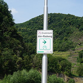 Ersatzroute Ahr-Radweg in Bad Neuenahr-Ahrweiler mit Wegweiser vor grünem Bergpanorama,