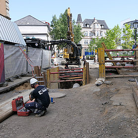 Arbeiter mit Werkzeugkasten auf dem Boden neben einer Leiter und einem Wiederbunt Bauzaunbanner.