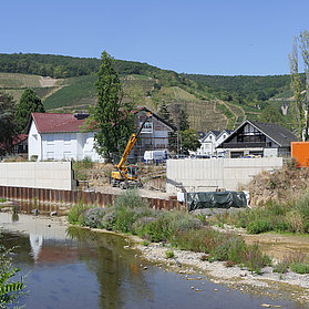 Betonwand und Baukran hinter der Ahr vor grünen Weinbergen.