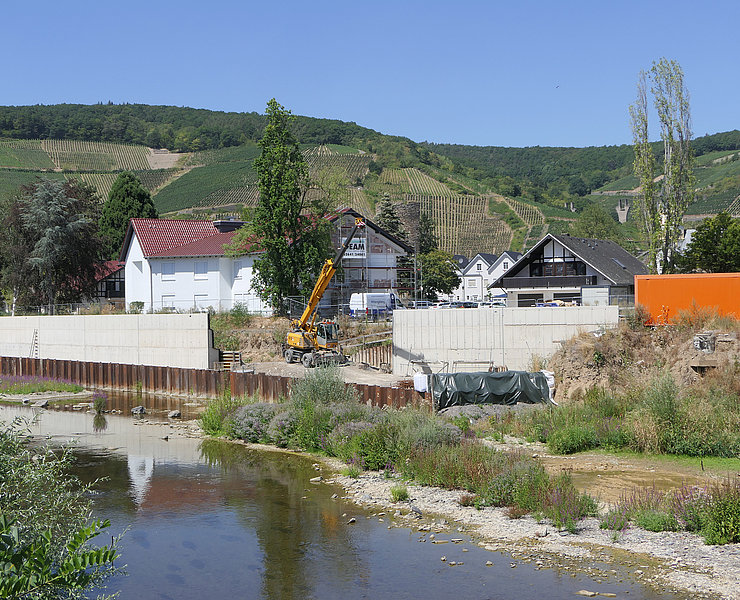 Betonwand und Baukran hinter der Ahr vor grünen Weinbergen.