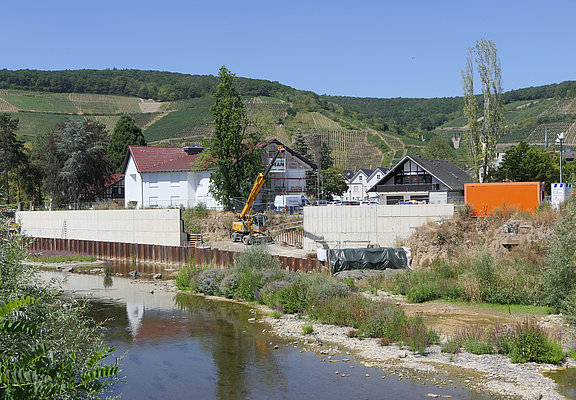 Betonwand und Baukran hinter der Ahr vor grünen Weinbergen.