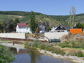 Betonwand und Baukran hinter der Ahr vor grünen Weinbergen.
